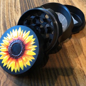 Pu&ograve; includere: Un macinino in metallo nero con un design a girasole sulla parte superiore. Il macinino &egrave; composto da quattro parti, tra cui un coperchio, una camera di macinazione, un setaccio e un fondo.