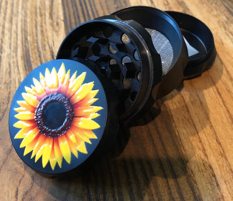 Pu&ograve; includere: Un macinino in metallo nero con un design a girasole sulla parte superiore. Il macinino &egrave; composto da quattro parti, tra cui un coperchio, una camera di macinazione, un setaccio e un fondo.