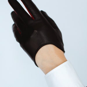 May include: Black leather driving gloves with red stitching. The gloves are fingerless and have a cuff.
