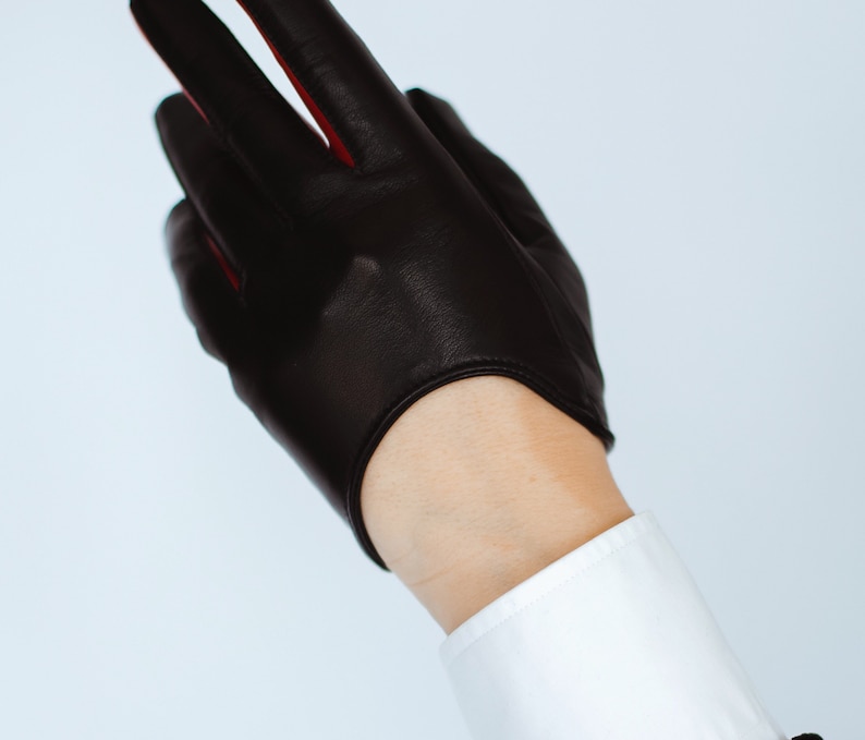 May include: Black leather driving gloves with red stitching. The gloves are fingerless and have a cuff.