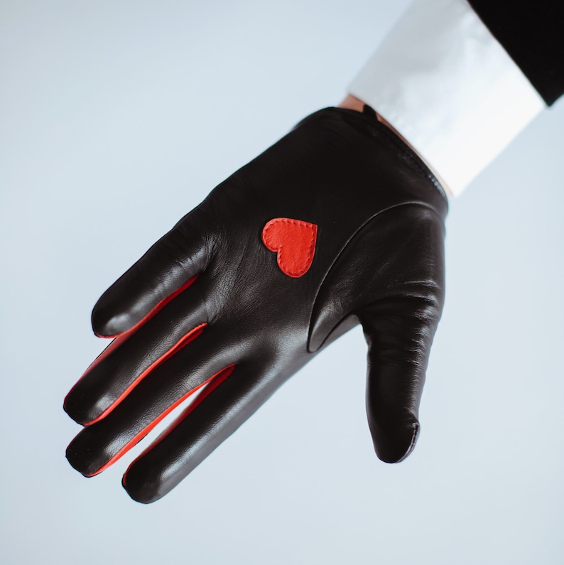 May include: A black leather driving glove with a red heart on the back of the hand.