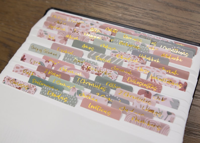 Peut inclure: Un ensemble d'onglets color&eacute;s &agrave; motifs floraux avec des lettres dor&eacute;es pour une Bible. Les onglets comprennent les noms des livres de la Bible tels que Gen&egrave;se, Exode, L&eacute;vitique, Nombres, Deut&eacute;ronome, Josu&eacute;, Juges, Ruth, 1 Samuel, 2 Samuel, 1 Rois, 2 Rois, 1 Chroniques, 2 Chroniques, Esdras, N&eacute;h&eacute;mie, Esther, Job, Psaumes, Proverbes, Eccl&eacute;siaste, Cantique des Cantiques, Isa&iuml;e, J&eacute;r&eacute;mie, Lamentations, &Eacute;z&eacute;chiel, Daniel, Os&eacute;e, Jo&euml;l, Amos, Abdias, Jonas, Mich&eacute;e, Nahum, Habacuc, Sophonie, Agg&eacute;e, Zacharie, Malachie.
