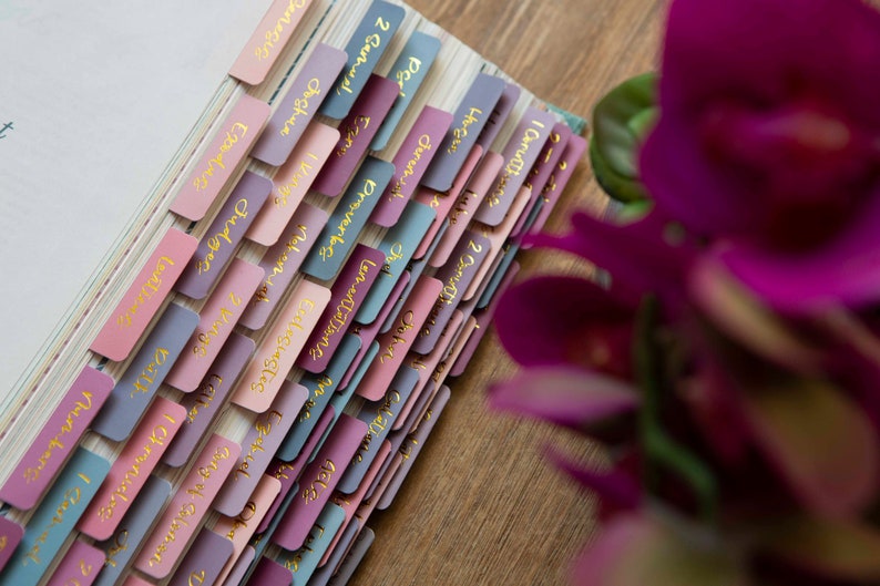 May include: A close-up of a book with colorful tabs labeled with names in gold lettering. The tabs are arranged in a stack, with the top tab labeled "I Carutthin".