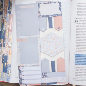 May include: A close-up of a Bible open to Isaiah 55, with several floral patterned sticky notes and tabs. The sticky notes are in shades of blue and pink. The tabs are in shades of pink and blue with gold lettering. The text on the page reads "Come to the Lord" and "Seek the Lord while he may be found".