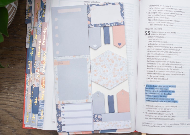 May include: A close-up of a Bible open to Isaiah 55, with several floral patterned sticky notes and tabs. The sticky notes are in shades of blue and pink. The tabs are in shades of pink and blue with gold lettering. The text on the page reads "Come to the Lord" and "Seek the Lord while he may be found".