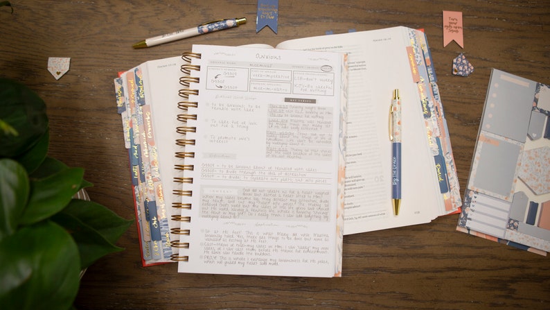 bible-journal-with-word-study-on-anxiety-laying-on-open-bible-with-peach-and-blue-bible-tabs