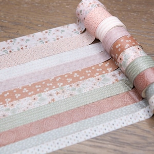 Pode incluir: Uma cole&ccedil;&atilde;o de rolos de fita washi decorativa em v&aacute;rias cores pastel e padr&otilde;es. Os designs incluem padr&otilde;es florais, de bolinhas e listrados. A fita est&aacute; desenrolada, mostrando os diferentes designs. Os rolos est&atilde;o em uma superf&iacute;cie de madeira.
