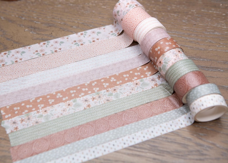 Pode incluir: Uma cole&ccedil;&atilde;o de rolos de fita washi decorativa em v&aacute;rias cores pastel e padr&otilde;es. Os designs incluem padr&otilde;es florais, de bolinhas e listrados. A fita est&aacute; desenrolada, mostrando os diferentes designs. Os rolos est&atilde;o em uma superf&iacute;cie de madeira.