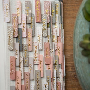 May include: A set of colorful book tabs with gold lettering, featuring names of books from the Bible, including Genesis, Exodus, Leviticus, Numbers, Deuteronomy, Joshua, Judges, Ruth, 1 Samuel, 2 Samuel, 1 Kings, 2 Kings, 1 Chronicles, 2 Chronicles, Ezra, Nehemiah, Esther, Job, Psalms, Proverbs, Ecclesiastes, Song of Solomon, Isaiah, Jeremiah, Lamentations, Ezekiel, Daniel, Hosea, Joel, Amos, Obadiah, Jonah, Micah, Nahum, Habakkuk, Zephaniah, Haggai, Zechariah, Malachi, Matthew, Mark, Luke, John, Acts, Romans, 1 Corinthians, 2 Corinthians, Galatians, Ephesians, Philippians, Colossians, 1 Thessalonians, 2 Thessalonians, 1 Timothy, 2 Timothy, Titus, Philemon, Hebrews, James, 1 Peter, 2 Peter, 1 John, 2 John, 3 John, Jude, and Revelation.