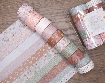 May include: A collection of decorative washi tape rolls in various pastel colors, including pink, brown, and green, with floral and patterned designs. Some rolls are arranged in a spiral, while others are laid out flat. The packaging includes the text "Selahi Washi Tape."