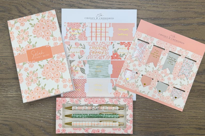 May include: A stationery set featuring a floral notebook labeled Selah Sticky Notes, a sheet of peach and green patterned adhesive tabs, a set of eight magnetic bookmarks with floral and solid designs, and three pens in a floral box by Chosen & Cherished.