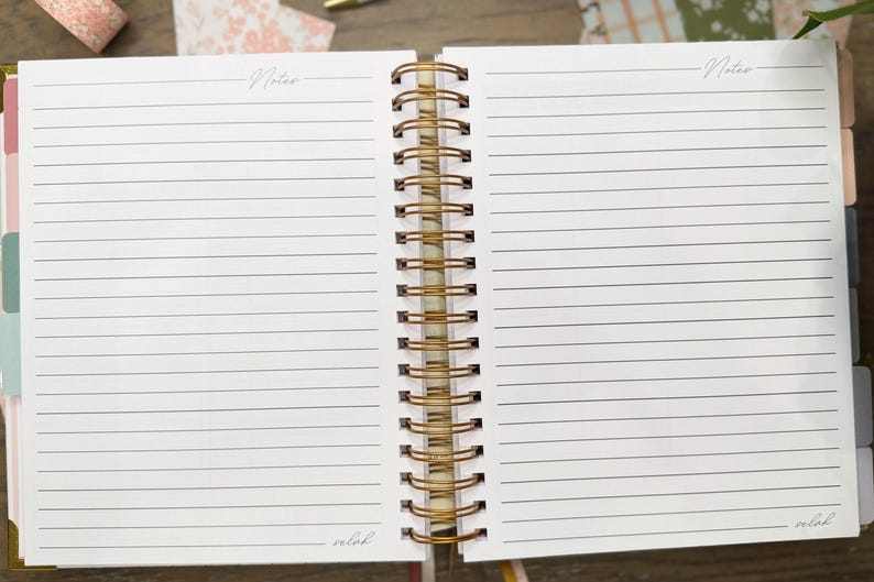 May include: An open spiral-bound notebook with white lined pages. Each page features the word Notes at the top and the word selah at the bottom. The binding is a metallic gold wire coil. The notebook includes colorful tabbed dividers on the side.