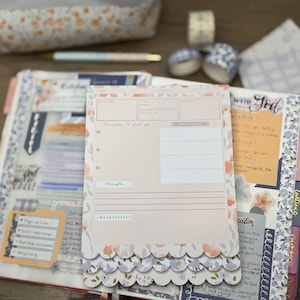 May include: A planner with a pink and floral design, open to a page with a pink paper insert. The insert has a scalloped edge and the text "Principles to Live By". Decorative tape, a pen, and a pencil case are in the background.