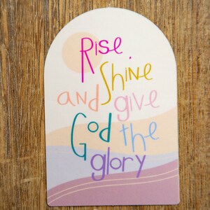 May include: A pink, white, and yellow arched sign with the text "Rise and shine and give God the glory".