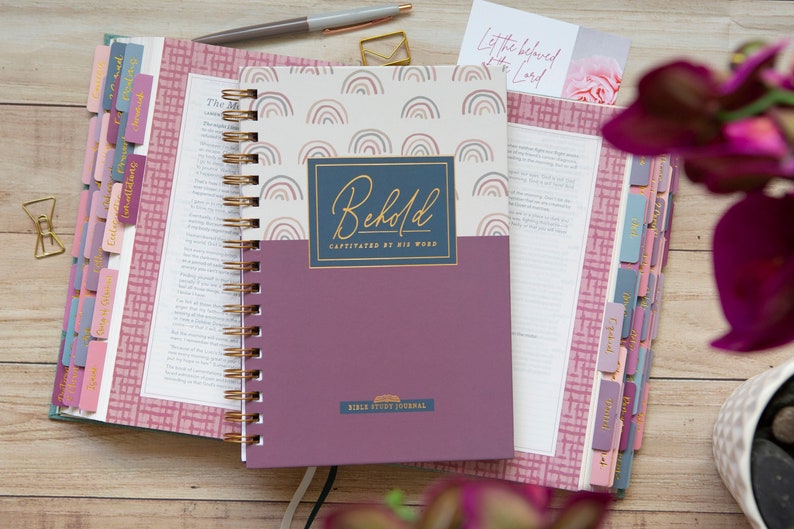 bible-journal-for-verse-by-verse-bible-study-with-rainbows-on-hard-cover-laying-on-open-bible-with-ombre-bible-tabs-and-cursive-gold-lettering