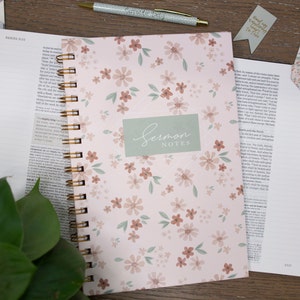 May include: A pink floral journal with a gold spiral binding. The cover has a green label that says "Sermon Notes".