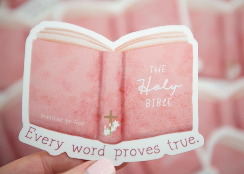 May include: A pink watercolor sticker of an open book with the words "The Holy Bible" and "Every word proves true." The sticker has a gold cross and flowers on the front cover.