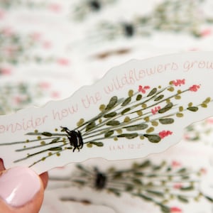 May include: A white sticker with a watercolor illustration of a bouquet of wildflowers. The sticker has the text "consider how the wildflowers grow" and "Luke 12:27" in pink lettering.