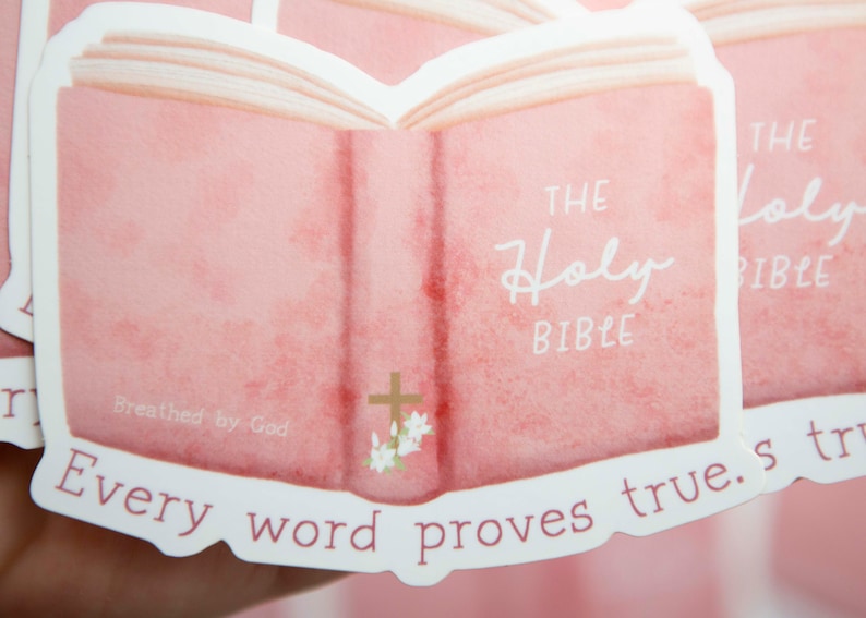 May include: A pink sticker with an open book illustration. The book has the words "The Holy Bible" written on it. The sticker also has the text "Breathed by God" and "Every word proves true."