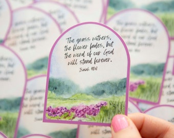 May include: A watercolor sticker with a purple flower field and a quote from Isaiah 40:8: "The grass withers, the flower fades, but the word of our God will stand forever."
