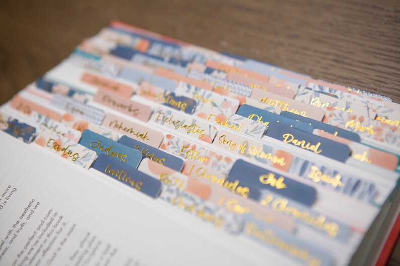 May include: A set of colorful, floral patterned tabs for a Bible or other book. The tabs are labeled with the names of books of the Bible, including Genesis, Exodus, Leviticus, Numbers, Deuteronomy, Joshua, Judges, Ruth, 1 Samuel, 2 Samuel, 1 Kings, 2 Kings, 1 Chronicles, 2 Chronicles, Ezra, Nehemiah, Esther, Job, Psalms, Proverbs, Ecclesiastes, Song of Solomon, Isaiah, Jeremiah, Lamentations, Ezekiel, Daniel, Hosea, Joel, Amos, Obadiah, Jonah, Micah, Nahum, Habakkuk, Zephaniah, Haggai, Zechariah, Malachi, Matthew, Mark, Luke, John, Acts, Romans, 1 Corinthians, 2 Corinthians, Galatians, Ephesians, Philippians, Colossians, 1 Thessalonians, 2 Thessalonians, 1 Timothy, 2 Timothy, Titus, Philemon, Hebrews, James, 1 Peter, 2 Peter, 1 John, 2 John, 3 John, Jude, and Revelation.