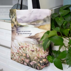 Puede incluir: Una bolsa de tela blanca con un dise&ntilde;o de paisaje de acuarela. La bolsa tiene un asa negra y el texto "New mercies every morning" impreso en la parte delantera.