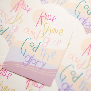 May include: A set of colorful cards with the phrase "Rise and Shine, Give God the Glory" written in a whimsical font. The cards have a pastel color scheme and feature a wavy design.