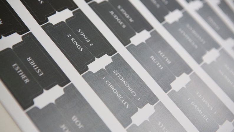 May include: Close-up of a set of gray and black book dividers with the names of books of the Bible printed on them, including 1 Samuel, Ruth, 1 Chronicles, 2 Kings, Judges, and Esther.
