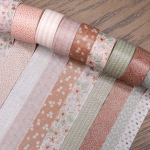 Pode incluir: Uma cole&ccedil;&atilde;o de rolos de fita washi decorativa em v&aacute;rios designs florais e estampados. A paleta de cores inclui tons de rosa, castanho e verde. A fita &eacute; desenrolada para mostrar os padr&otilde;es.