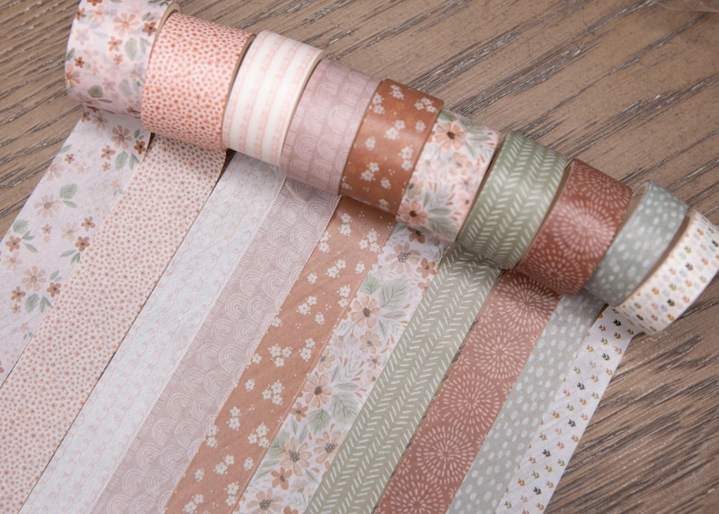 Pode incluir: Uma cole&ccedil;&atilde;o de rolos de fita washi decorativa em v&aacute;rios designs florais e estampados. A paleta de cores inclui tons de rosa, castanho e verde. A fita &eacute; desenrolada para mostrar os padr&otilde;es.