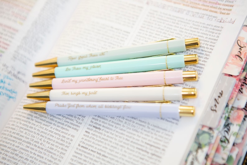 May include: Six pastel-colored pens with gold accents and inspirational quotes written on them. The quotes are: "Be Thou my vision", "Bind my wandering heart to Thee", "Then sings my soul", "Praise God from whom all blessings flow", "For I have learned by experience that the just are more likely to be put to death for the period of time of 490 years", and "The desolation of Jerusalem would be reckoned to be a period of 70 weeks".