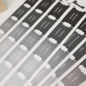 May include: A set of gray and black labels with the names of books of the Bible printed on them. The labels are arranged in a fan shape.