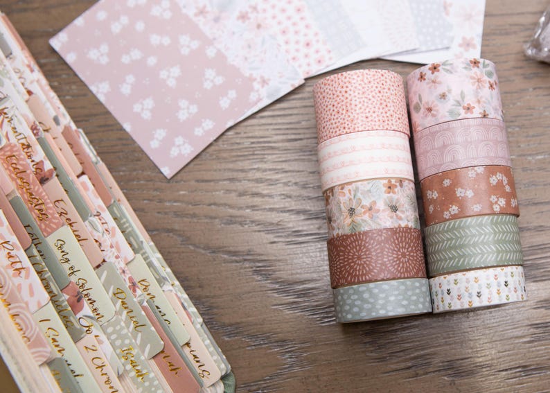 Pode incluir: Uma variedade de rolos de fita washi decorativa em v&aacute;rios designs florais e estampados, incluindo rosa, castanho e verde. Tamb&eacute;m s&atilde;o vis&iacute;veis folhas de papel coordenadas e um caderno com abas rotuladas, ideal para artesanato.