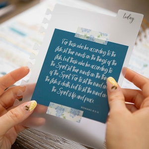 May include: A blue card with a white inspirational quote from Romans 8:6. The quote reads "For those who live according to the flesh set their minds on the things of the flesh, but those who live according to the Spirit set their minds on the things of the Spirit. For to set the mind on the flesh is death, but to set the mind on the Spirit is life and peace."