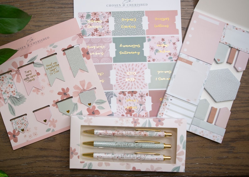 Peut inclure: Un ensemble de fournitures de papeterie &agrave; th&egrave;me floral rose et vert. L'ensemble comprend un paquet de signets, un paquet d'autocollants, un paquet de notes adh&eacute;sives et trois stylos. Les stylos ont un motif floral et le texte "Our Hope is Built on Nothing Less" imprim&eacute; dessus.