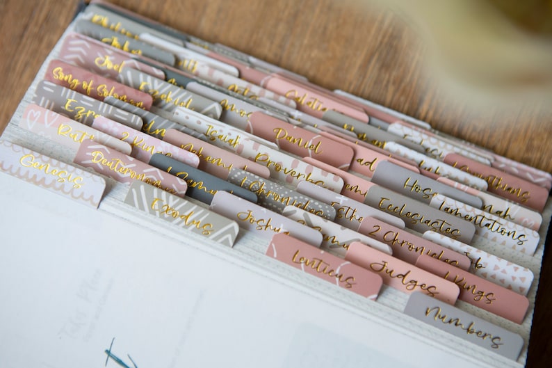 May include: A set of colorful, patterned tabs for a Bible. The tabs are labeled with the names of the books of the Bible, including Genesis, Exodus, Leviticus, Numbers, Deuteronomy, Joshua, Judges, Ruth, 1 Samuel, 2 Samuel, 1 Kings, 2 Kings, 1 Chronicles, 2 Chronicles, Ezra, Nehemiah, Esther, Job, Psalms, Proverbs, Ecclesiastes, Song of Solomon, Isaiah, Jeremiah, Lamentations, Ezekiel, Daniel, Hosea, Joel, Amos, Obadiah, Jonah, Micah, Nahum, Habakkuk, Zephaniah, Haggai, Zechariah, Malachi, Matthew, Mark, Luke, John, Acts, Romans, 1 Corinthians, 2 Corinthians, Galatians, Ephesians, Philippians, Colossians, 1 Thessalonians, 2 Thessalonians, 1 Timothy, 2 Timothy, Titus, Philemon, Hebrews, James, 1 Peter, 2 Peter, 1 John, 2 John, 3 John, Jude, and Revelation.