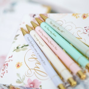 May include: Set of six pastel colored pens with gold accents and inspirational quotes engraved on each pen. The quotes are: "How Great Thou Art", "Be Thou My Vision", "Bind my wandering heart to Thee", "Then sing my soul", "Praise God from whom all blessings flow", and "I know".