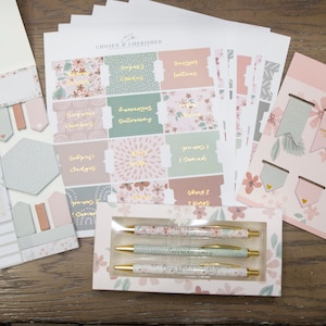 Peut inclure: Un ensemble de fournitures de papeterie &agrave; th&egrave;me floral rose et vert comprenant des autocollants, des blocs-notes, des stylos et des signets. Les autocollants pr&eacute;sentent des versets bibliques et le texte "Chosen & Cherished".