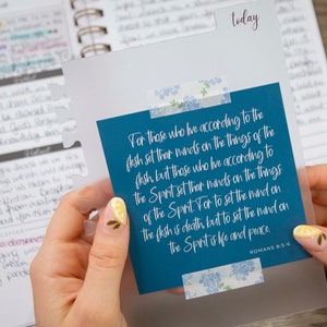 May include: A blue card with a white border and floral patterned tape. The card has a quote from Romans 8:6: "For those who live according to the flesh set their minds on the things of the flesh, but those who live according to the Spirit set their minds on the things of the Spirit. For to set the mind on the flesh is death, but to set the mind on the Spirit is life and peace."