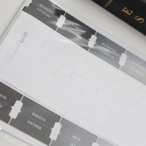 May include: A set of black and white Bible book tabs with the names of the books printed on them. The tabs are in a clear plastic bag and say "Reference Guide" on the top.