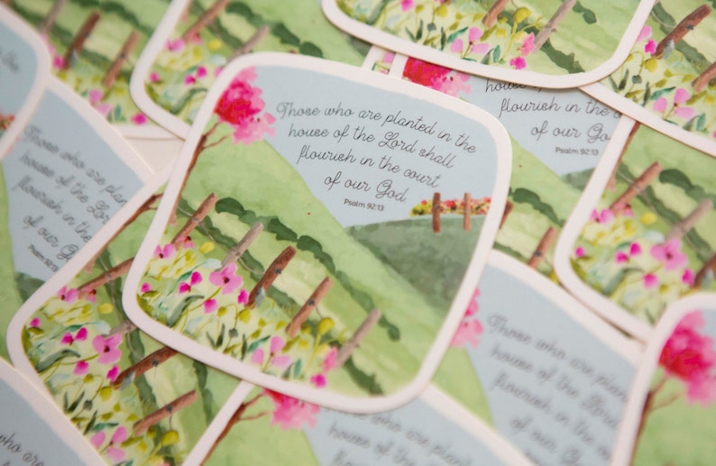 May include: A stack of green and white cards with a watercolor illustration of a field with pink flowers and a blue sky. The text on the card reads "Those who are planted in the house of the Lord shall flourish in the court of our God. Psalm 92:13."