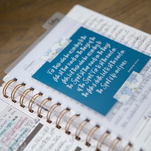 May include: A blue and white inspirational quote card with the text "For those who he according to the flesh set their minds on the things of the flesh, but those who be according to the Spirit set their minds on the things of the Spirit. For to set the mind on the flesh is death, but to set the mind on the Spirit is life and peace."  The quote is from Romans 8:6.