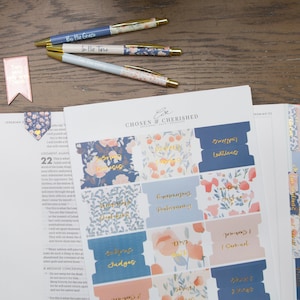 May include: A set of blue and pink floral patterned stickers for a bible. The stickers have gold lettering and include phrases like "Praying for You" and "Stepping into Faith".