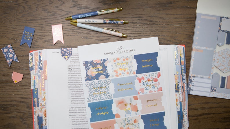 May include: A set of blue and pink floral patterned stickers for a bible. The stickers have gold lettering and include phrases like "Praying for You" and "Stepping into Faith".