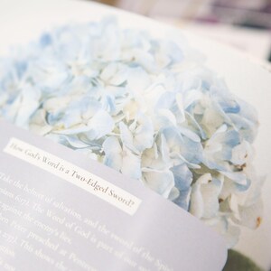 May include: Open book with a light blue hydrangea flower image. Text on a white label reads "How God's Word is a Two-Edged Sword?" The book pages have additional text in a light gray font.
