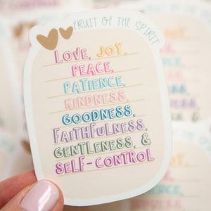 May include: A sticker with a peach background and a white border. The sticker features a mason jar with the text "FRUIT OF THE SPIRIT" at the top. The jar is filled with the words "LOVE, JOY, PEACE, PATIENCE, KINDNESS, GOODNESS, FAITHFULNESS, GENTLENESS, & SELF-CONTROL" in different colors.