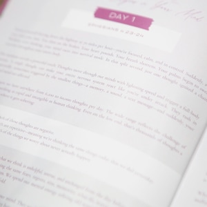 May include: Open book with text on white pages. The top of the page has a pink banner that says "DAY 1". The text is in a light gray color. The book is open to a page with text about thoughts and the mind.