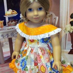 May include: A doll wearing a floral print dress with a yellow collar and ruffled hem. The dress features a white bow and is paired with white shoes. The doll has blonde hair and blue eyes.