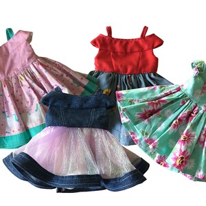 May include: Four colorful doll dresses. One pink dress with a unicorn pattern, a red dress, a denim dress with a pink tulle skirt, and a turquoise dress with a floral pattern. Each dress has a unique design.