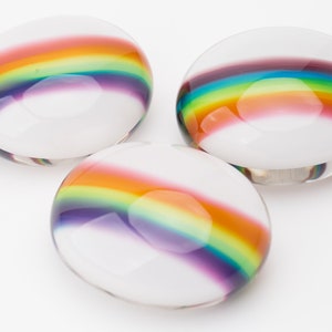 May include: Three round glass paperweights with a rainbow design. The paperweights are clear glass with a rainbow stripe across the centre.